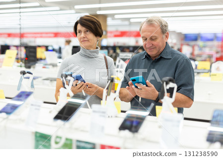 Mature couple diligently choosing smartphone in hypermarket 131238590