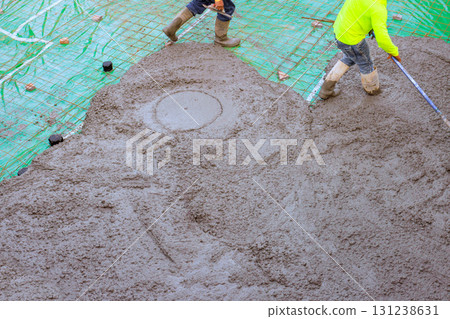 Workers in pouring fresh concrete mix spread for base foundation on construction site. 131238631