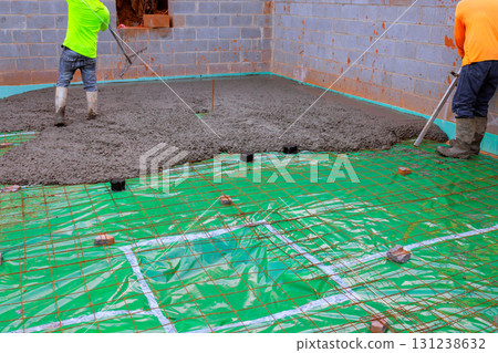 Workers pour wet concrete onto slab covered with protective sheet, ensuring precise placement. Workers pour wet concrete onto slab covered with protective sheet, ensuring precise placement. 131238632