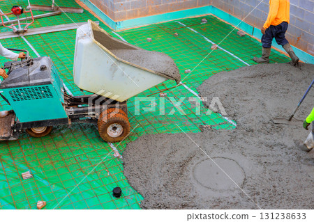 Workers are pouring fresh concrete on base foundation wheeled concrete wheelbarrow usage at construction site. 131238633