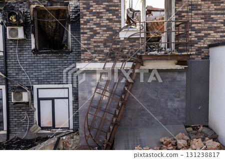 War. The aftermath of Russian airstrikes on a peaceful Ukrainian city. A hospital and a recreation center were destroyed. Fire damaged brick building with collapsed metal staircase and debris. 131238817