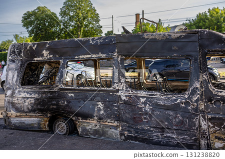 War. The aftermath of Russian airstrikes on a peaceful Ukrainian city. Charred minibus with gutted interior, melted tires, exposed seat frames on pavement, with cars, trees, and traffic behind. War. The aftermath of Russian airstrikes on a peaceful Ukrainian city. Charred minibus with gutted interior, melted tires, exposed seat frames on pavement, with cars, trees, and traffic behind. 131238820