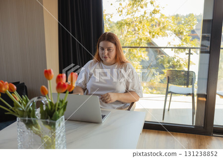Woman working remotely on laptop at home office near window Woman working remotely on laptop at home office near window 131238852