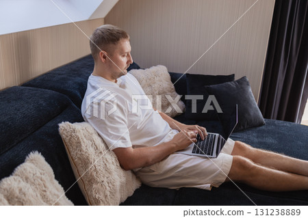Man working on laptop and using smartphone while sitting on sofa at home. Concept of freelancing, digital lifestyle, mobile technology, e-banking, online shopping, communication and productivity. Man working on laptop and using smartphone while sitting on sofa at home. Concept of freelancing, digital lifestyle, mobile technology, e-banking, online shopping, communication and productivity. 131238889