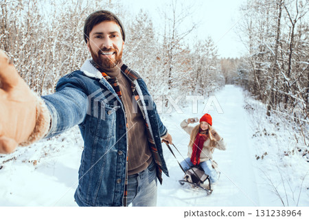 Dad pulling sled with his daughter on it in a winter forest 131238964