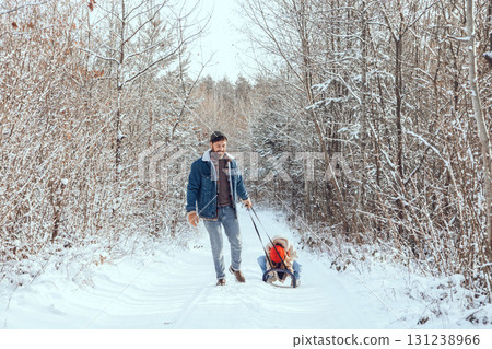 Dad pulling sled with his daughter on it in a winter forest 131238966