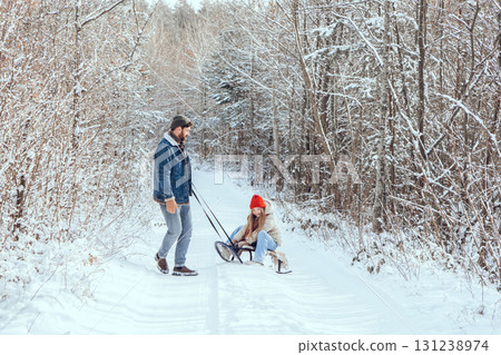 Dad pulling sled with his daughter on it in a winter forest Dad pulling sled with his daughter on it in a winter forest 131238974