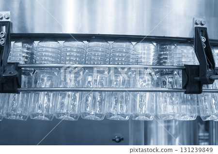 The empty drinking water bottles hanging on the overhead conveyor belt for filling process in the light blue scene. The empty drinking water bottles hanging on the overhead conveyor belt for filling process in the light blue scene. 131239849