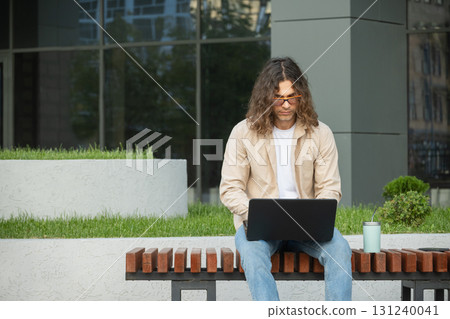 Man Using Laptop on Outdoor Bench for Remote Work Man Using Laptop on Outdoor Bench for Remote Work 131240041