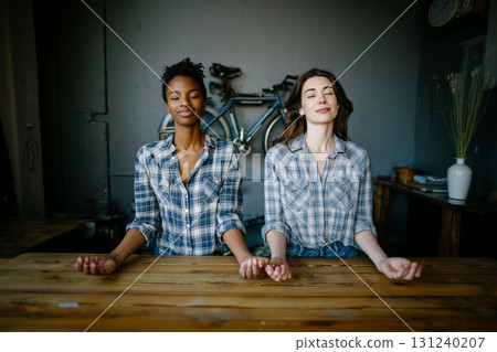 Two women are sitting at a table, one of them is wearing a plaid shirt 131240207