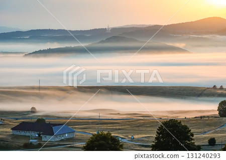 Foggy autumn morning in Zabljak, Montenegro, with a rustic house in the countryside. Golden sunrise lighting creates a cozy and atmospheric rural landscape. Perfect for travel, lifestyle, background 131240293