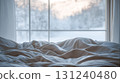 Messy cozy bed with rumpled sheets near large window overlooking peaceful snowy winter landscape 131240480