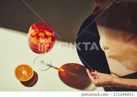 Aperol spritz with ice cubes on table beside vinyl record and orange slice Aperol spritz with ice cubes on table beside vinyl record and orange slice 131240851