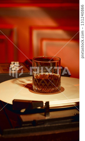 Glass of whiskey placed on vinyl record under warm red light 131240866
