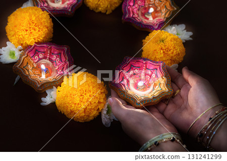 Hands holding Diwali candles with marigold flowers in a circle 131241299