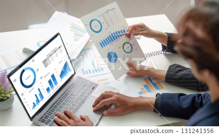 Collaborative Analysis. Professionals discussing financial data with reports and laptop. 131241356