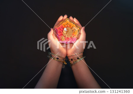 Hands holding a beautifully crafted Diwali candle with intricate design 131241360