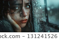 An artistic close-up of a woman's face, with water drops on a glass pane, creating a blurred and emotional effect 131241526