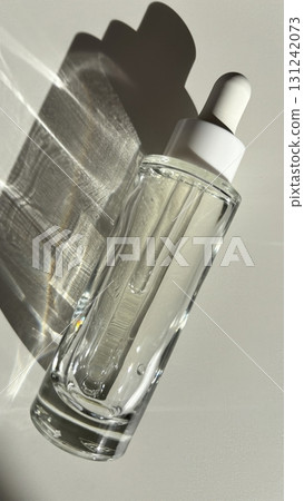 Glass cosmetic dropper bottle with serum on white background with sunlight and shadow minimalist skincare product mockup Glass cosmetic dropper bottle with serum on white background with sunlight and shadow minimalist skincare product mockup 131242073