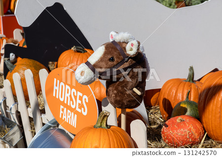 Charming brown hobby horse toy stands near a HORSES FARM sign, surrounded by vibrant autumn pumpkins, capturing seasonal harvest festival joy Charming brown hobby horse toy stands near a HORSES FARM sign, surrounded by vibrant autumn pumpkins, capturing seasonal harvest festival joy 131242570