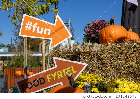 Arrow sign with fun text guides guests to an autumn festival, with pumpkins, hay, and flowers, conveying joyful harvest celebration Arrow sign with fun text guides guests to an autumn festival, with pumpkins, hay, and flowers, conveying joyful harvest celebration 131242573