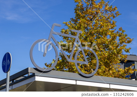 Prominent metal bicycle symbol on a modern building structure, representing urban sustainable transport, green mobility, and active cycling lifestyle Prominent metal bicycle symbol on a modern building structure, representing urban sustainable transport, green mobility, and active cycling lifestyle 131242606