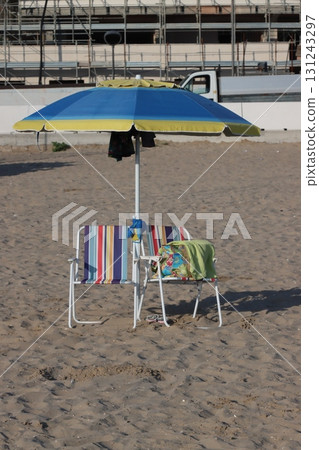 Beach umbrella and chairs standing on sandy beach near construction site 131243297