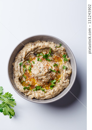 Baba ganoush - spread of baked eggplant with tahini and spices in gray bowl on white background. Baba ganoush - spread of baked eggplant with tahini and spices in gray bowl on white background. 131243902