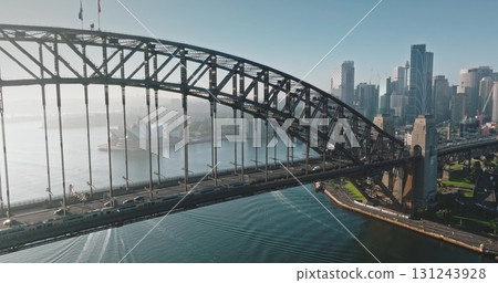 Australia, Sydney: Aerial view of Sydney Harbour Bridge, Sydney Opera House and city skyline in background. Sunny morning light, train and cars crossing the bridge. Modern architecture. Drone 131243928