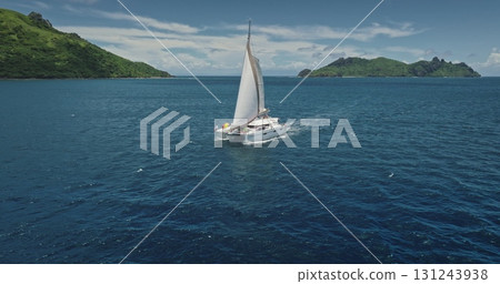 Fiji: Catamaran sailing blue ocean near tropical island on beautiful sunny day, offering perfect aerial view of dream vacation. Remote wild nature paradise, exotic summer travel. Drone flight Fiji: Catamaran sailing blue ocean near tropical island on beautiful sunny day, offering perfect aerial view of dream vacation. Remote wild nature paradise, exotic summer travel. Drone flight 131243938