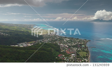 Breathtaking aerial view showcasing the vibrant coastline of Tahiti, where lush green volcanic hills meet the turquoise ocean waters, creating a mesmerizing tropical paradise under a cloudy sky 131243939