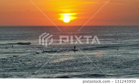 Surfers waiting for perfect wave at sunset in Bali, Indonesia, create striking silhouettes against a vibrant orange and yellow sky, essence of tropical paradise. Beautiful nature travel background 131243950