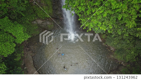 Fiji, Nadi Waterfall: picturesque waterfall cascades into a pool where tourists people swim and enjoy nature's beauty. Lush green tropical rainforest. Wild nature landscape. Drone flight 131243962