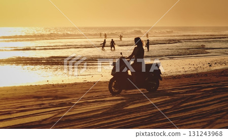 Silhouette of beautiful woman riding scooter along sandy beach, golden warm sunset over ocean waves in Bali, local fishermen fishing in background. Remote wild nature paradise, exotic summer travel 131243968