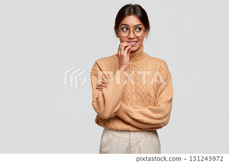 Young Woman in Cozy Sweater Smiling and Looking Thoughtful in Studio Setting During Daytime 131243972