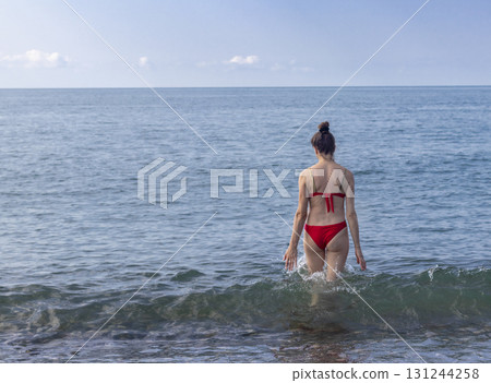 Attractive woman with long hair, wearing red bikini entering the sea Attractive woman with long hair, wearing red bikini entering the sea 131244258