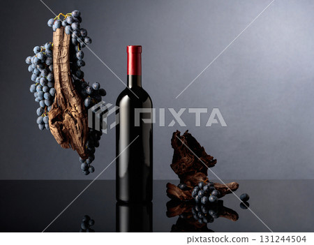 Bottle of red wine with a weathered snag and blue grapes on a black reflective background. Bottle of red wine with a weathered snag and blue grapes on a black reflective background. 131244504