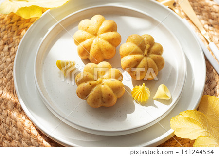 Pumpkin-Shaped Mini Cakes with Cream and Autumn Decor on Woven Placemat 131244534