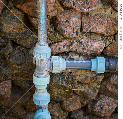Plastic water pipes with fittings installed on a wall made of large stones 131244955