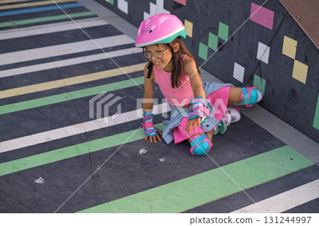 A beautiful girl in bright pink clothes gets up laughing after falling while roller skating A beautiful girl in bright pink clothes gets up laughing after falling while roller skating 131244997