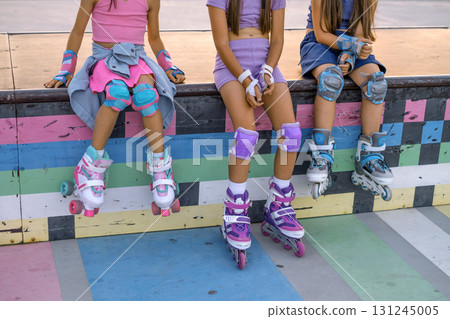 Three girls are sitting on the ramp of a city sports skate park, relaxing after roller skating 131245005