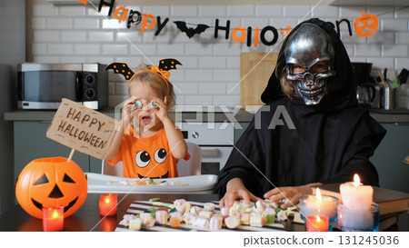 Children having fun while sitting at a table in a kitchen filled with colorful candies and decorations jack o lantern with sign Happy Halloween nearby Children having fun while sitting at a table in a kitchen filled with colorful candies and decorations jack o lantern with sign Happy Halloween nearby 131245036