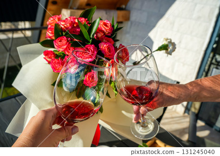 Close-up of two hands clinking wine glasses in a toast against a vibrant floral background. Perfect for romantic celebrations, lifestyle, and festive imagery. 131245040