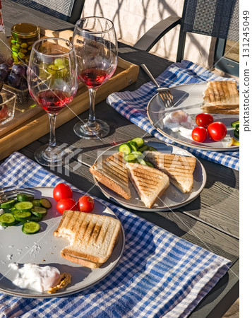 Rustic breakfast on a terrace including wine, homemade toasts with eggs and vegetables, fresh fruits, and blue checkered napkins. 131245049