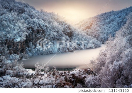 Scenic view of frozen ice lake and by snowy trees at sunset 131245160