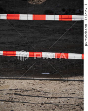 Fence with red and white stripes is in front of a dirt field 131245701