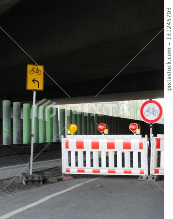 Yellow sign with a bike symbol on it is next to a red and white barrier 131245703
