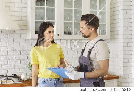 Young woman discussing contract details with professional handyman in kitchen 131245810