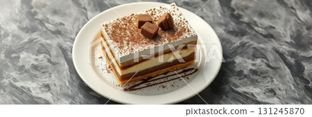 Delightful layered dessert served on a plate with chocolate and cream toppings, perfect for an afternoon treat 131245870