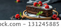 Delicious chocolate cake slice adorned with fresh raspberries and mint leaves on a wooden plate 131245885